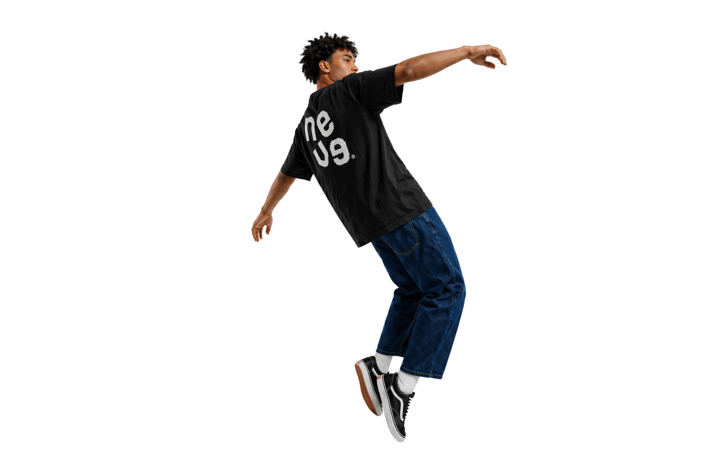A male model wearing an oversized black graphic t-shirt, loose blue denim shorts, white socks, and black sneakers, captured mid-air in a dynamic leaning pose against a plain grey background.